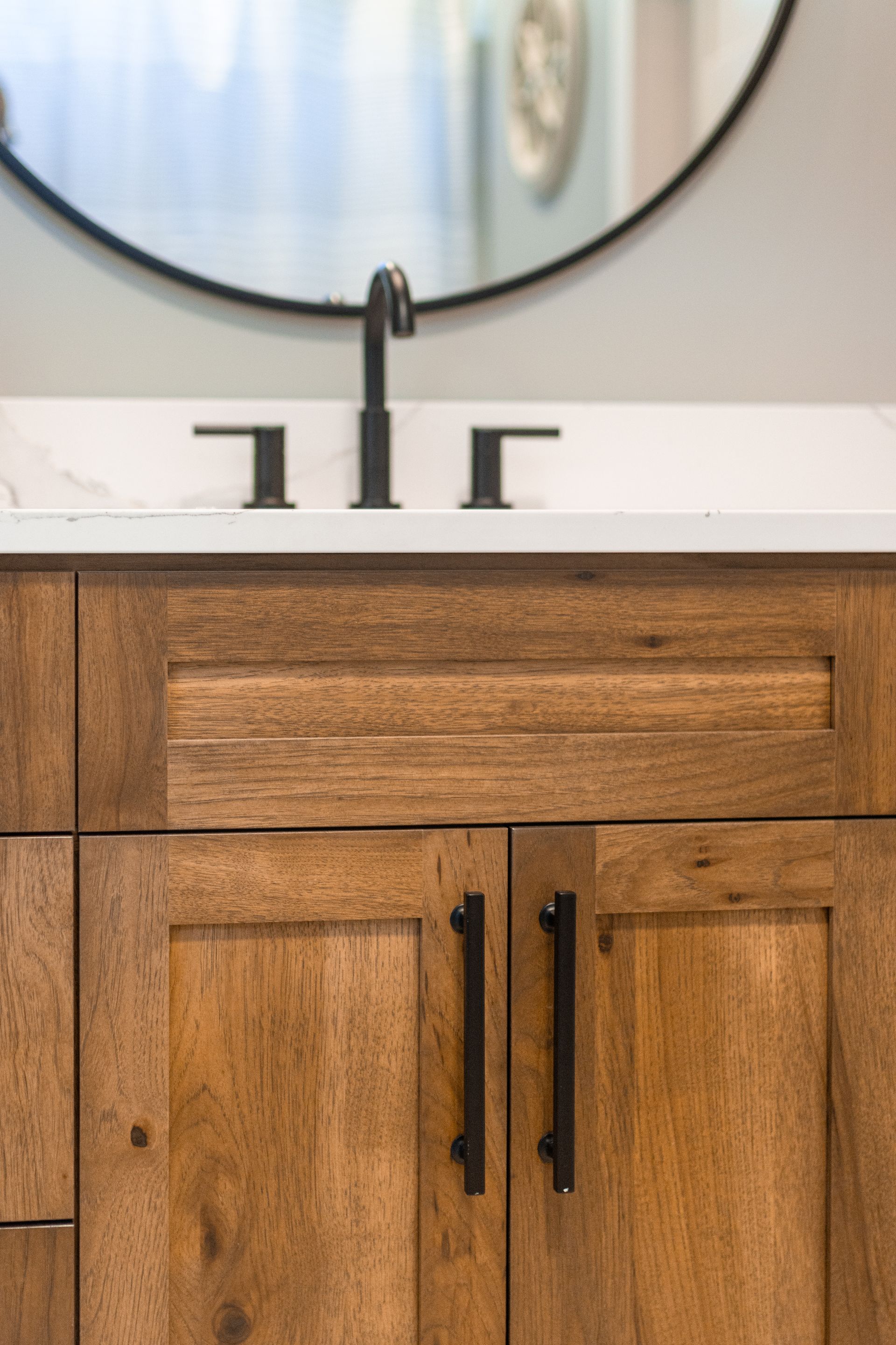 Wooden bathroom vanity with matte black faucet, pulls, and round mirror.