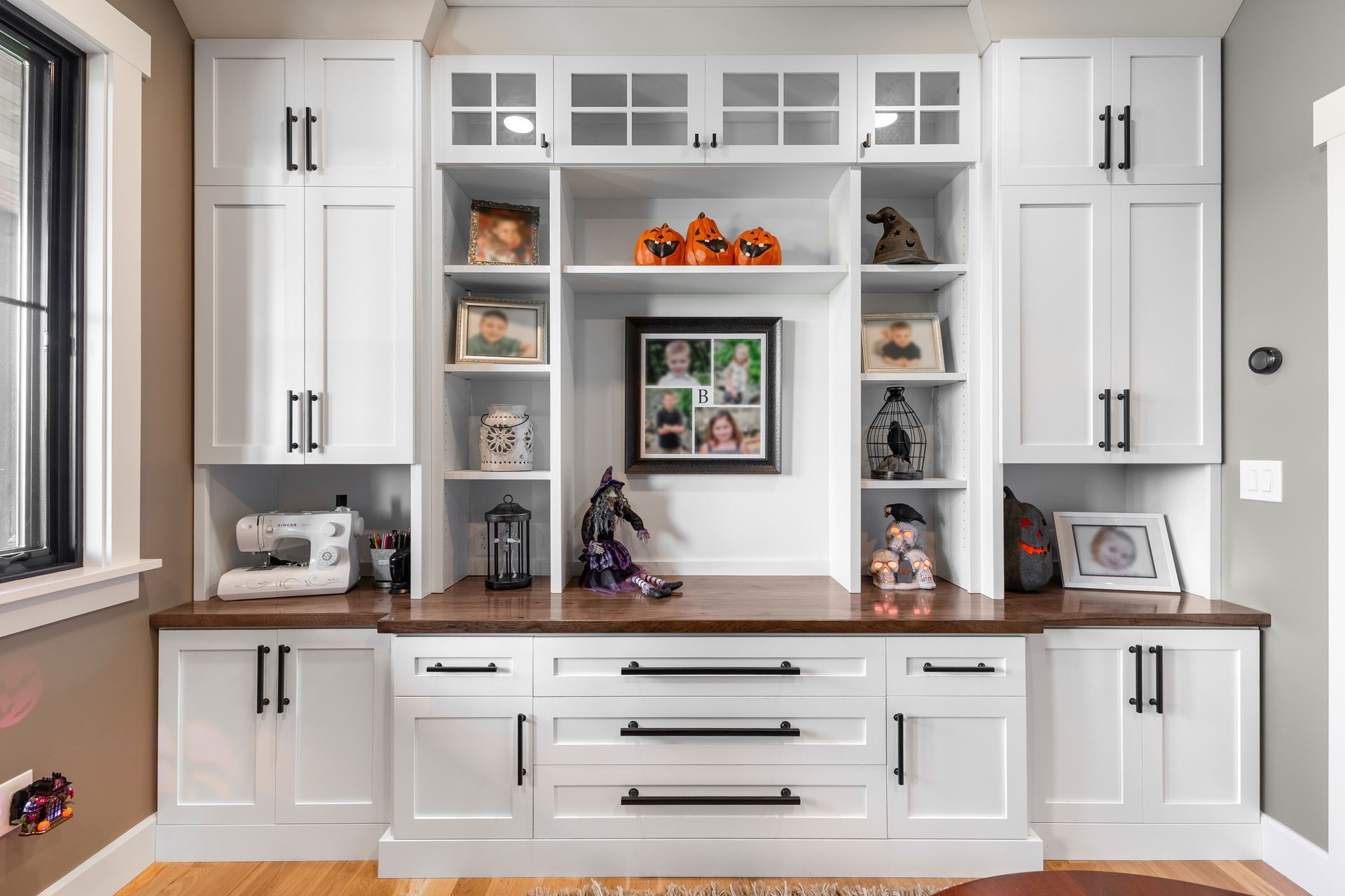 White built-in cabinet with desk and open shelving, displaying decorations and photos.