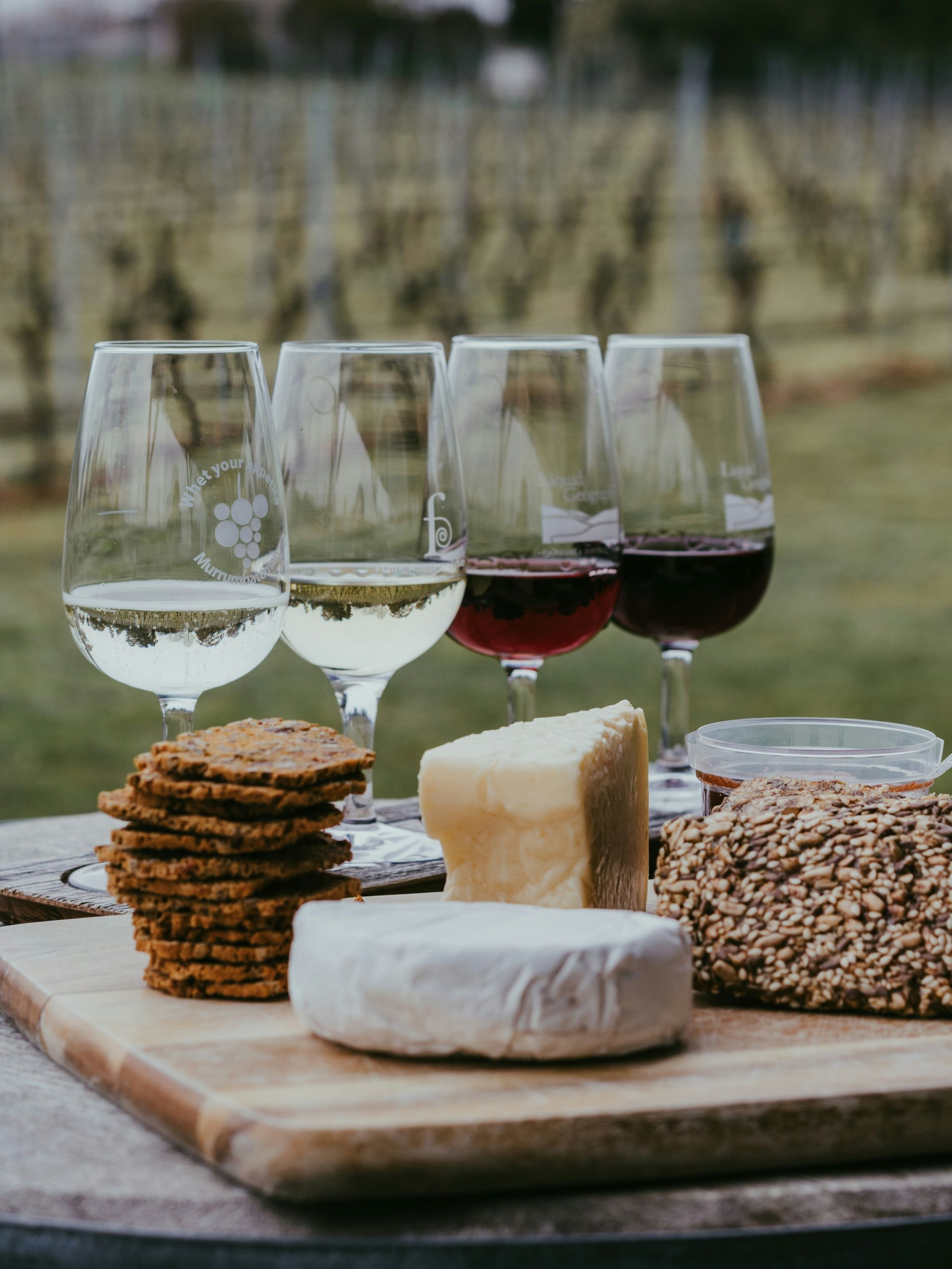 Wine glasses and assorted cheeses with crackers on a wooden board outdoors