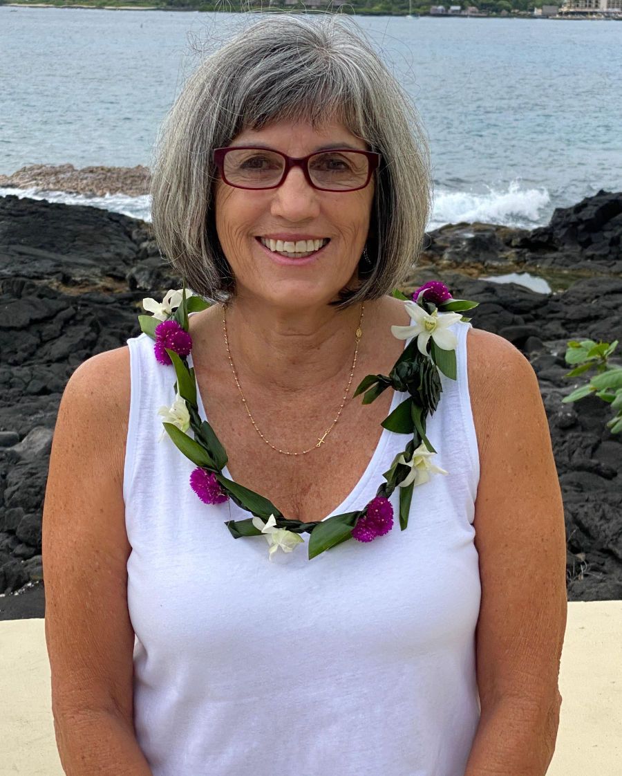 A woman wearing glasses and a lei is smiling for the camera.