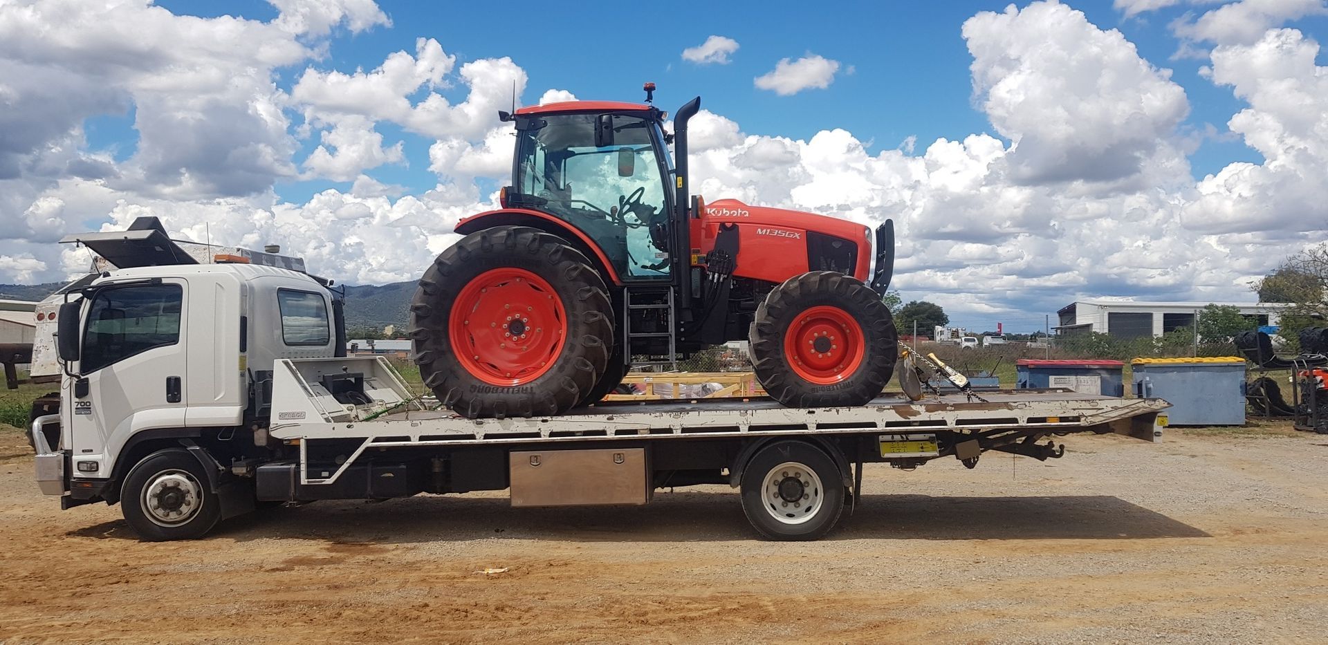 A red tractor is sitting on top of a flatbed tow truck.