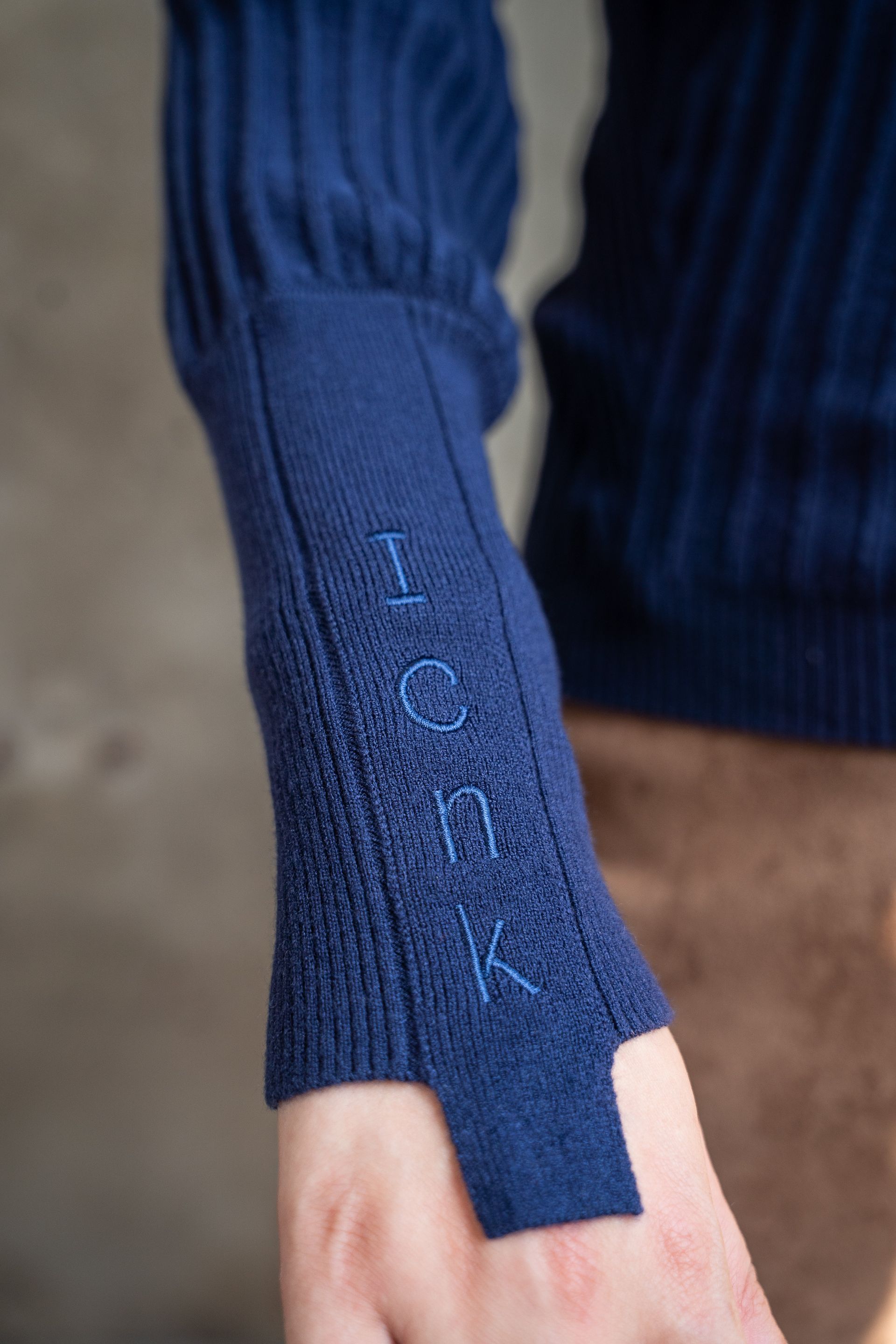 Detailopname van een blauwe truimouw met duimgat en ribgebreid detail.