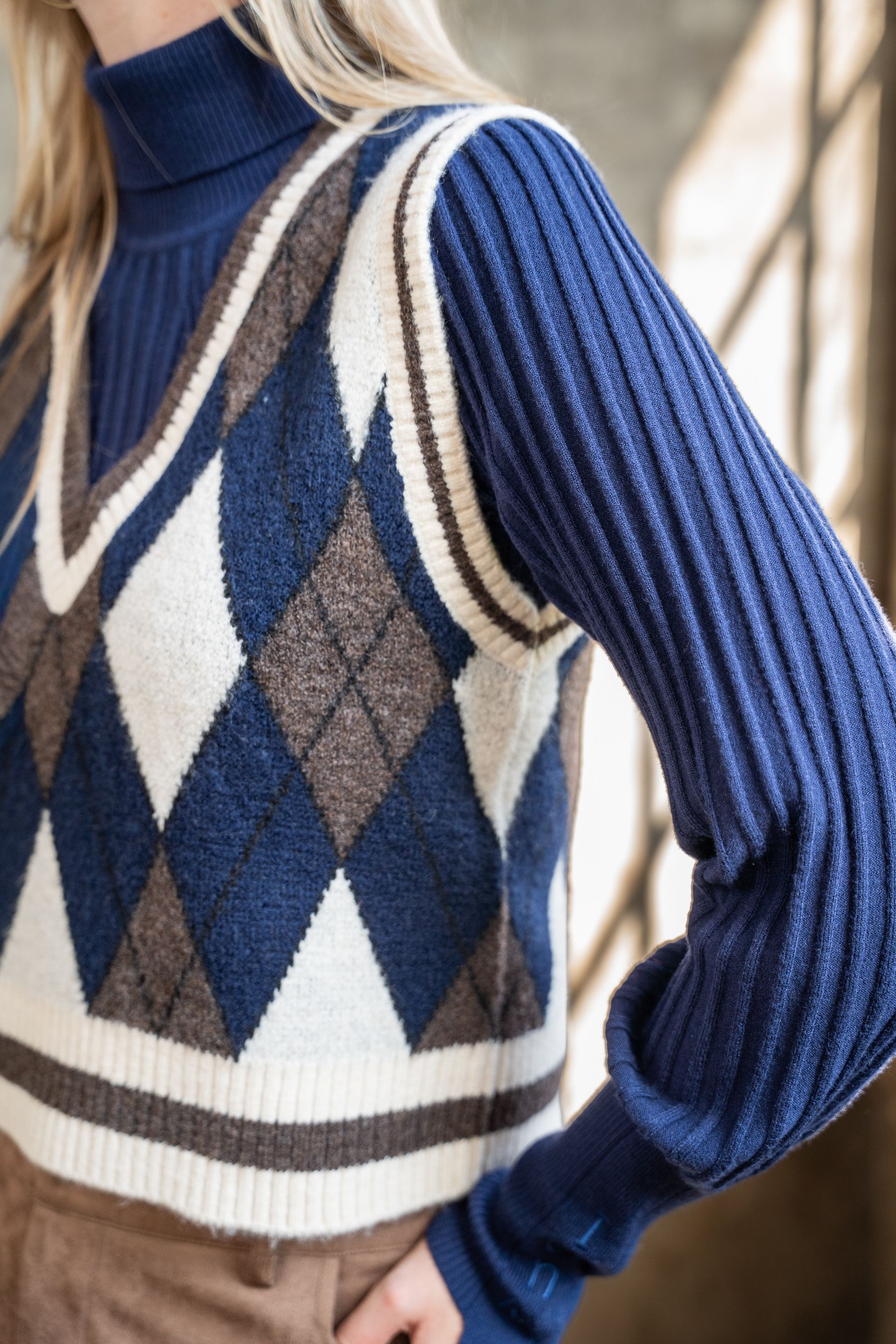 Een persoon buiten draagt ​​een blauw-crème argyle trui met geribbelde col en mouwen.