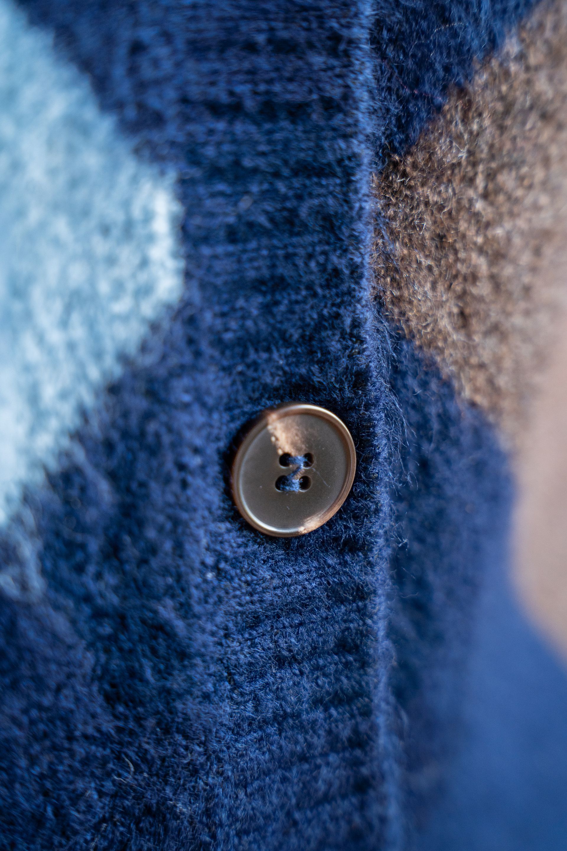 Close-up van een donkerblauwe gebreide vestknoop met een wazige blauw-beige achtergrond.