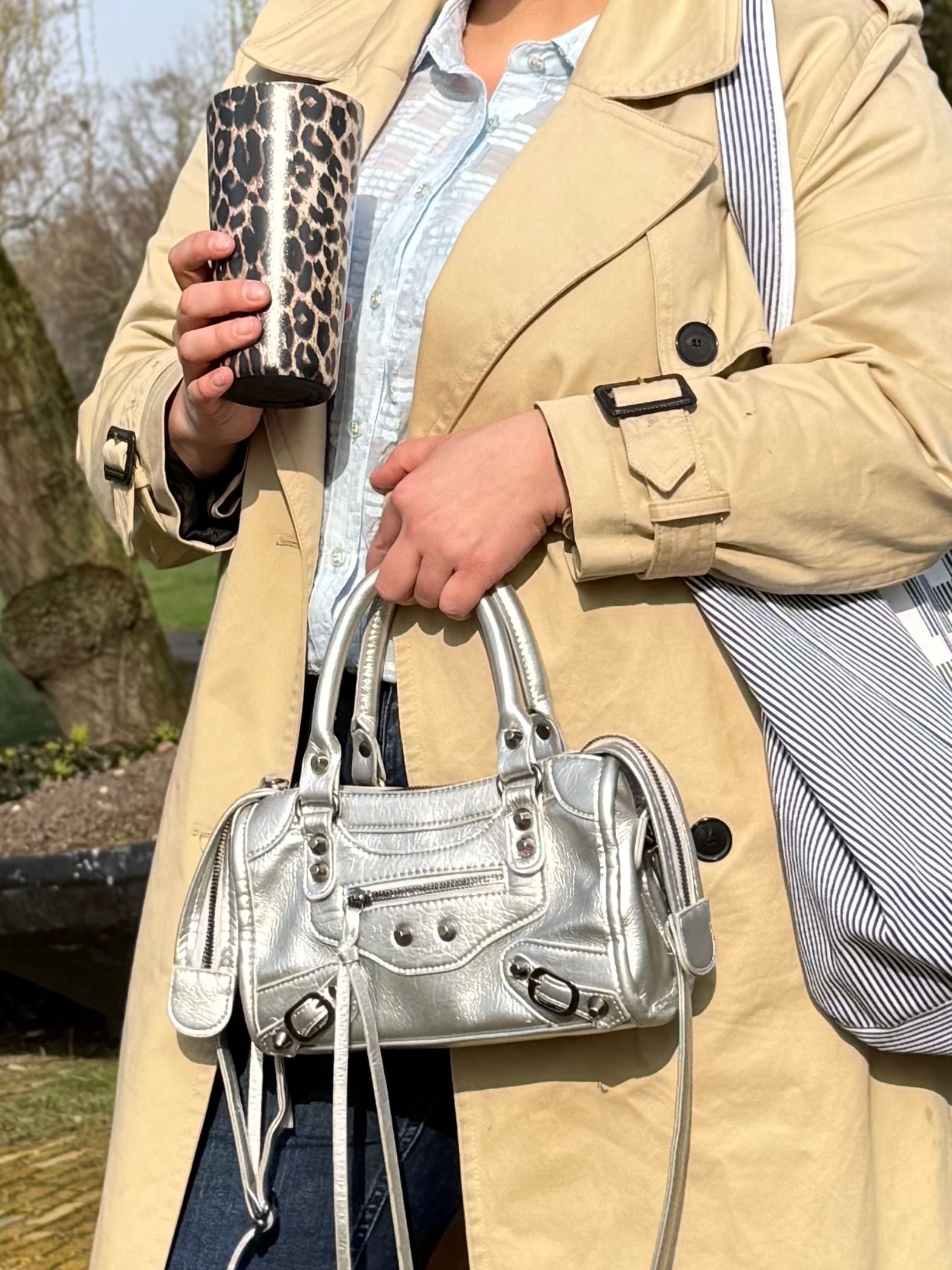 Persoon in beige jas met een zilveren handtas en een drinkglas met patroon.