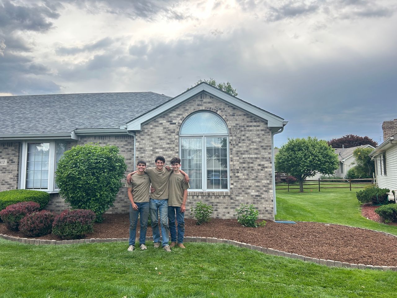 Three people with arms around each other in front of a house on a cloudy day. Three people with arms around each other in front of a house on a cloudy day.