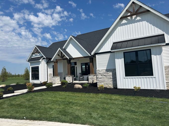 White house with black roof, trim, and windows, stone accents, and manicured landscaping under a blue sky.