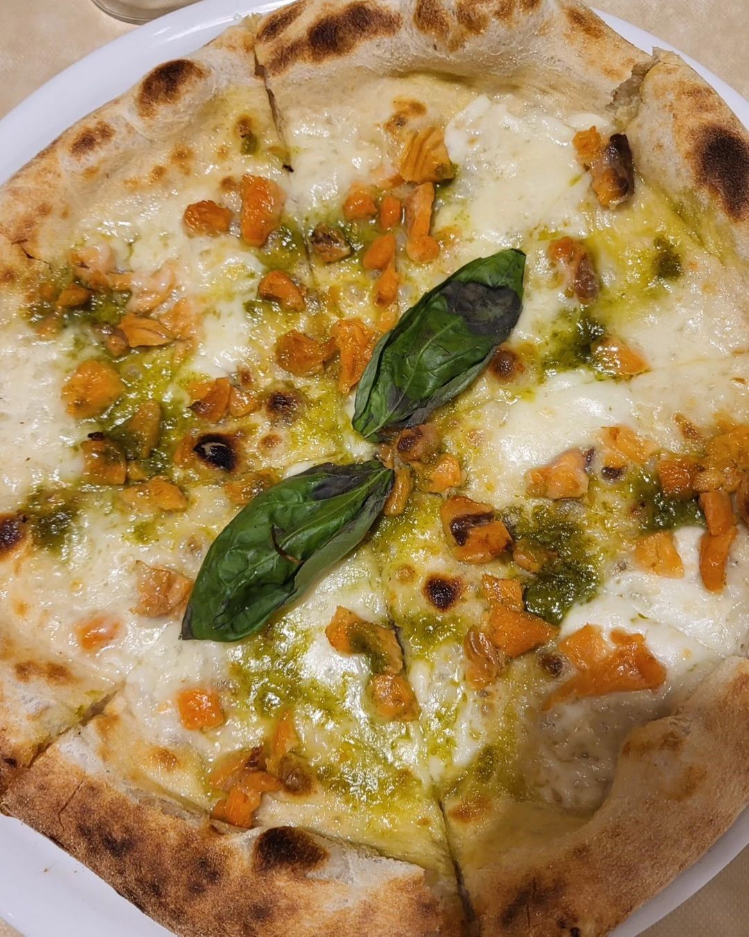 Pizza al formaggio con foglie di basilico e verdure a dadini su un piatto bianco.