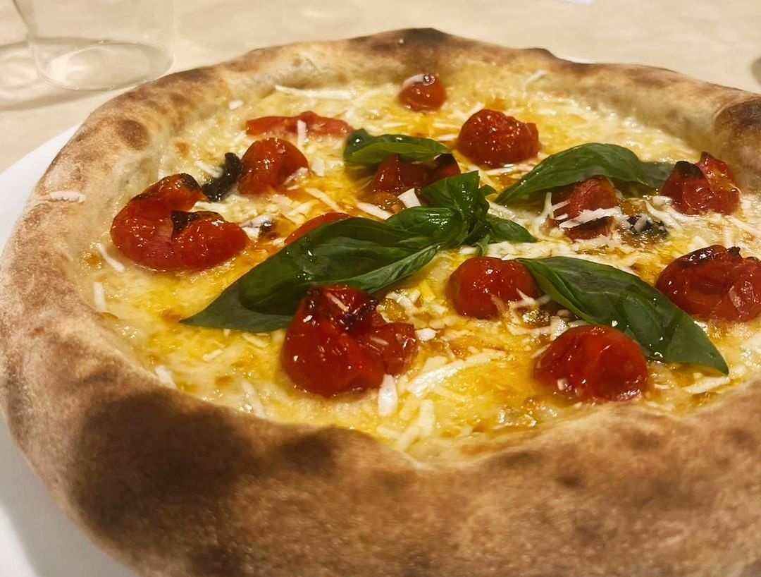 Pizza Margherita con foglie di basilico, formaggio fuso e pomodorini su un tagliere di legno.