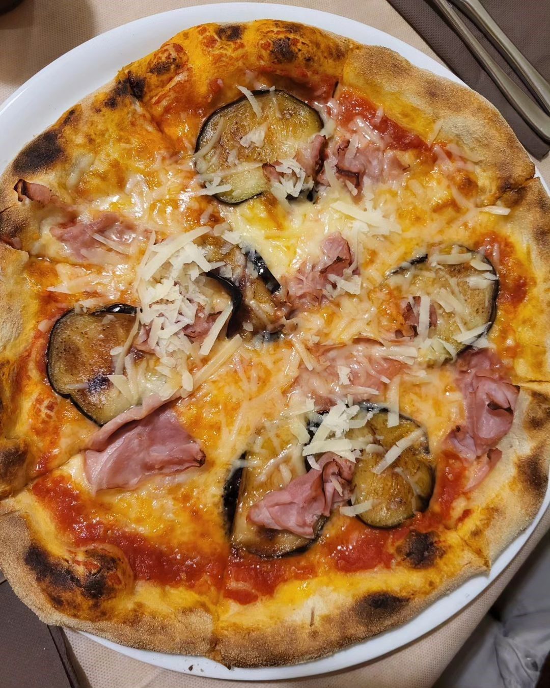 Pizza al formaggio con prosciutto e fette di melanzane arrostite su un piatto bianco