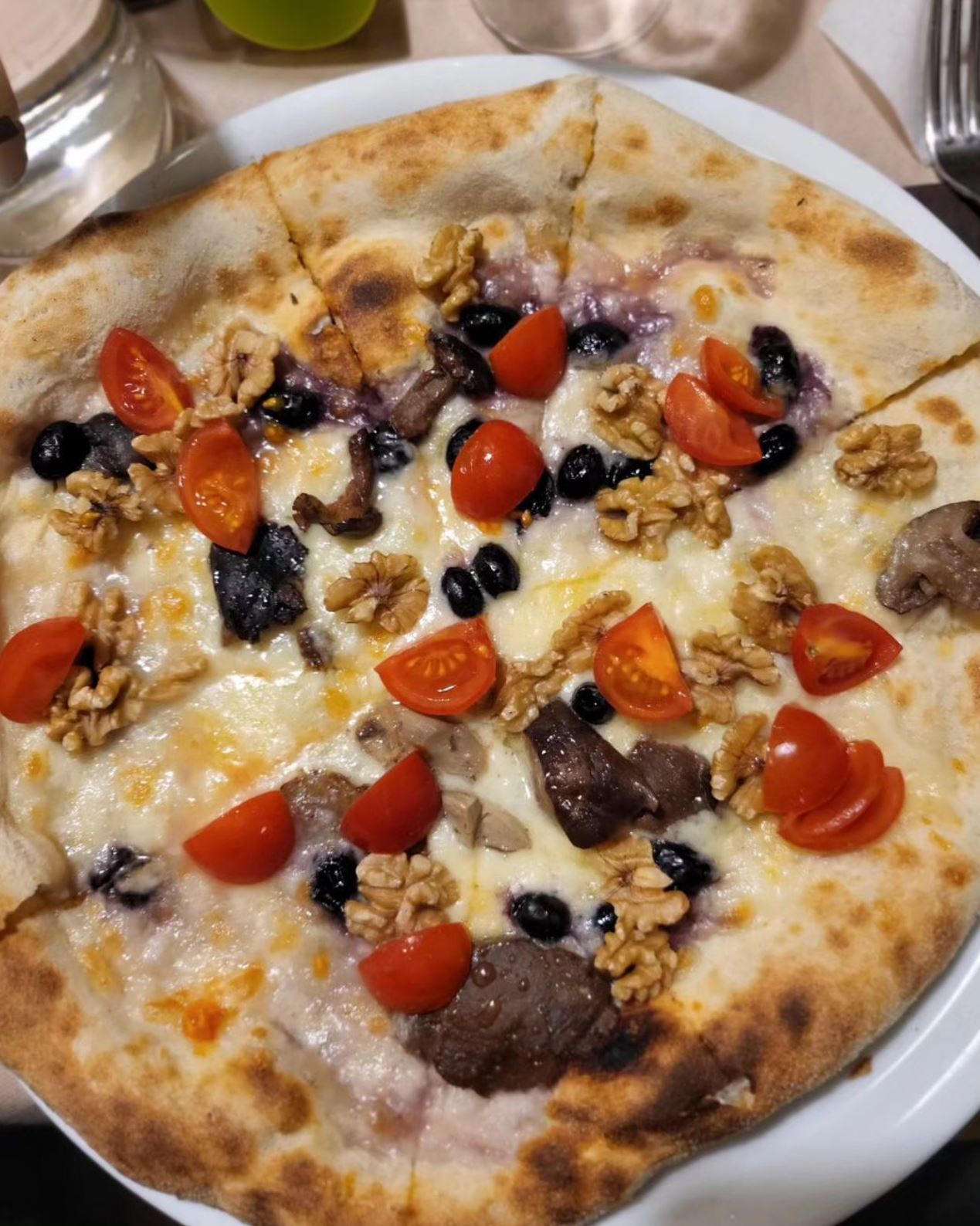 Pizza su pane piatto con pomodorini, olive, formaggio e carne su un piatto bianco