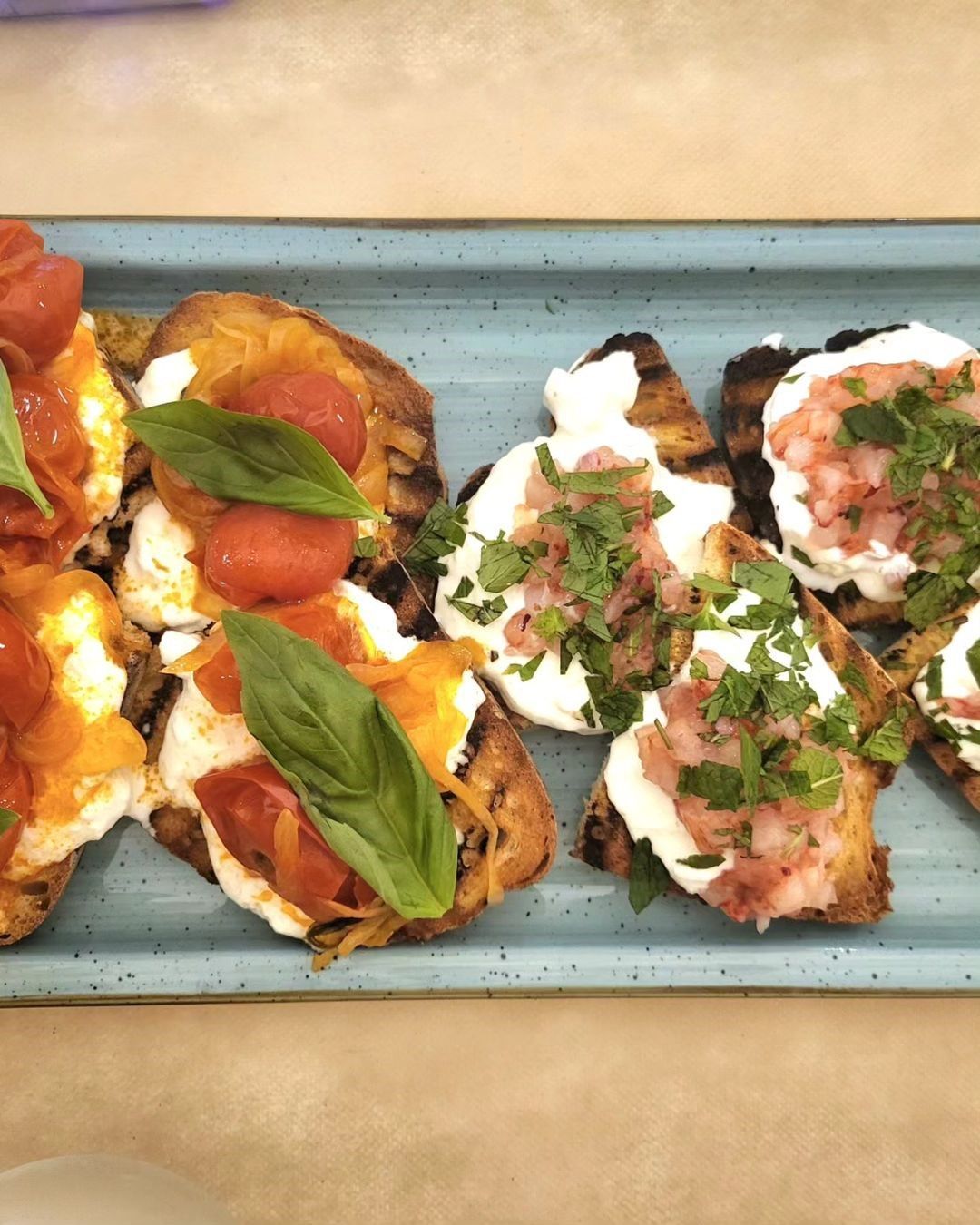 Bruschetta impiattata con pomodori, basilico e ricotta su un vassoio blu