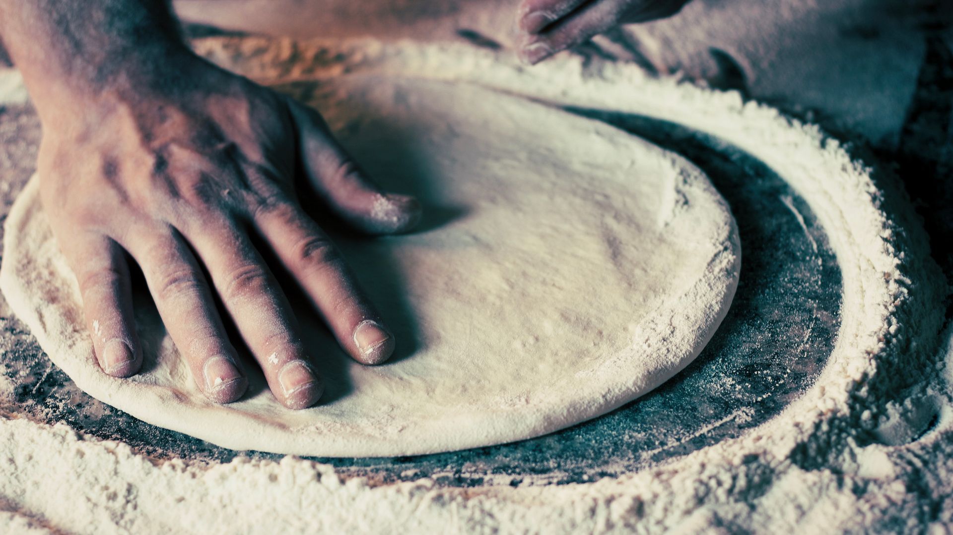 Una mano impasta la pasta su una superficie infarinata, formando una base rotonda per la pizza.