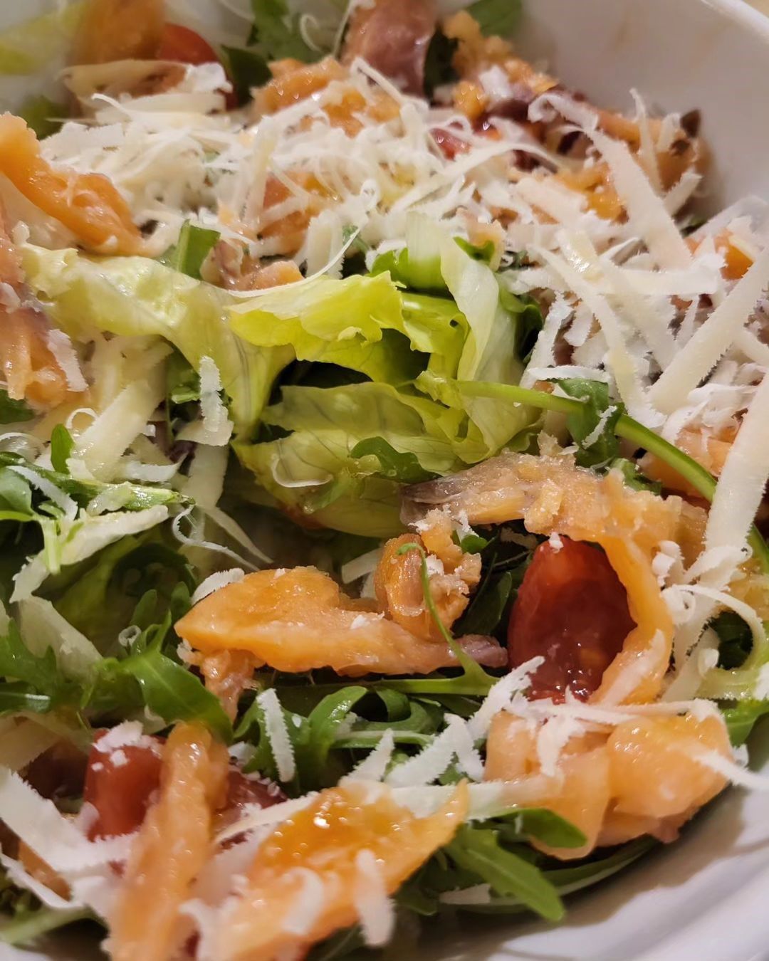 Insalata con verdure a foglia verde, salmone, pomodori e formaggio grattugiato in una ciotola bianca