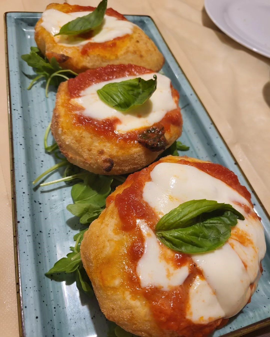 Tre mini pizze condite con salsa di pomodoro, formaggio fuso e basilico, servite su un piatto blu.