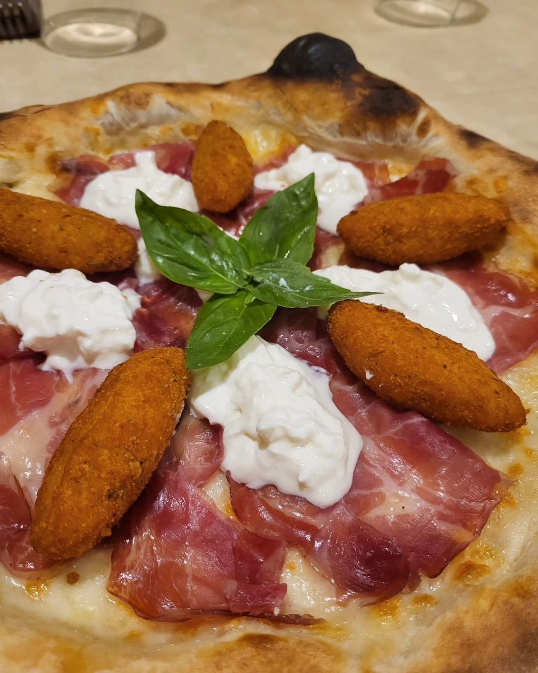 Pizza condita con basilico, prosciutto crudo, fiocchi di formaggio e crocchette fritte su un piatto