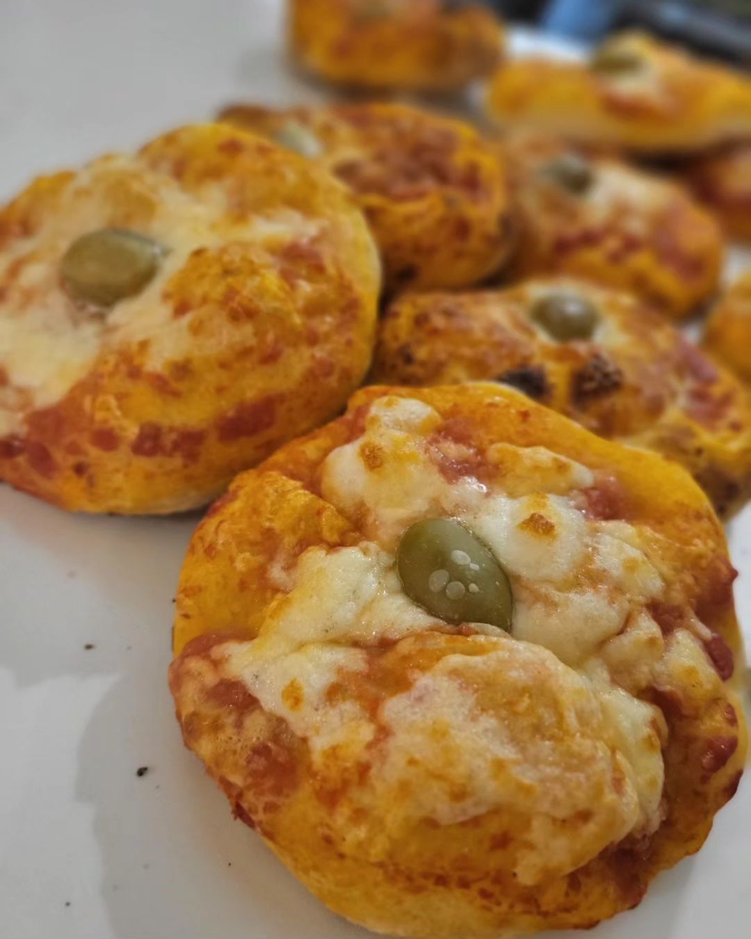Primo piano di mini pizze al forno con formaggio fuso e olive su un vassoio bianco.