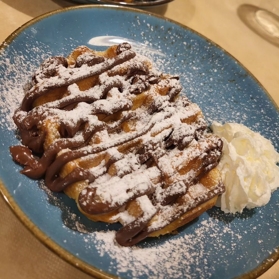 Crêpe dolce ricoperta di zucchero a velo su un piatto blu con panna montata a parte.