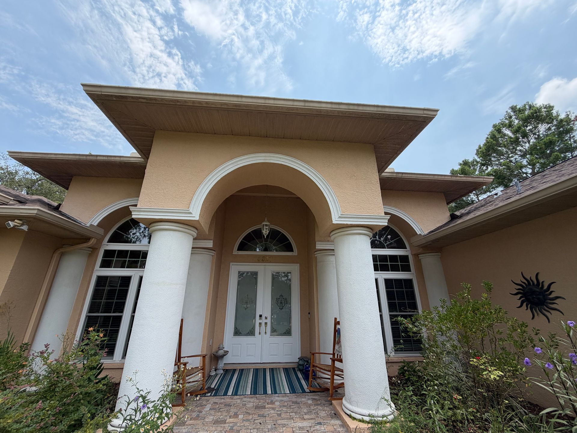 Front entrance of a beige stucco house with white columns and arched doorway under a blue sky