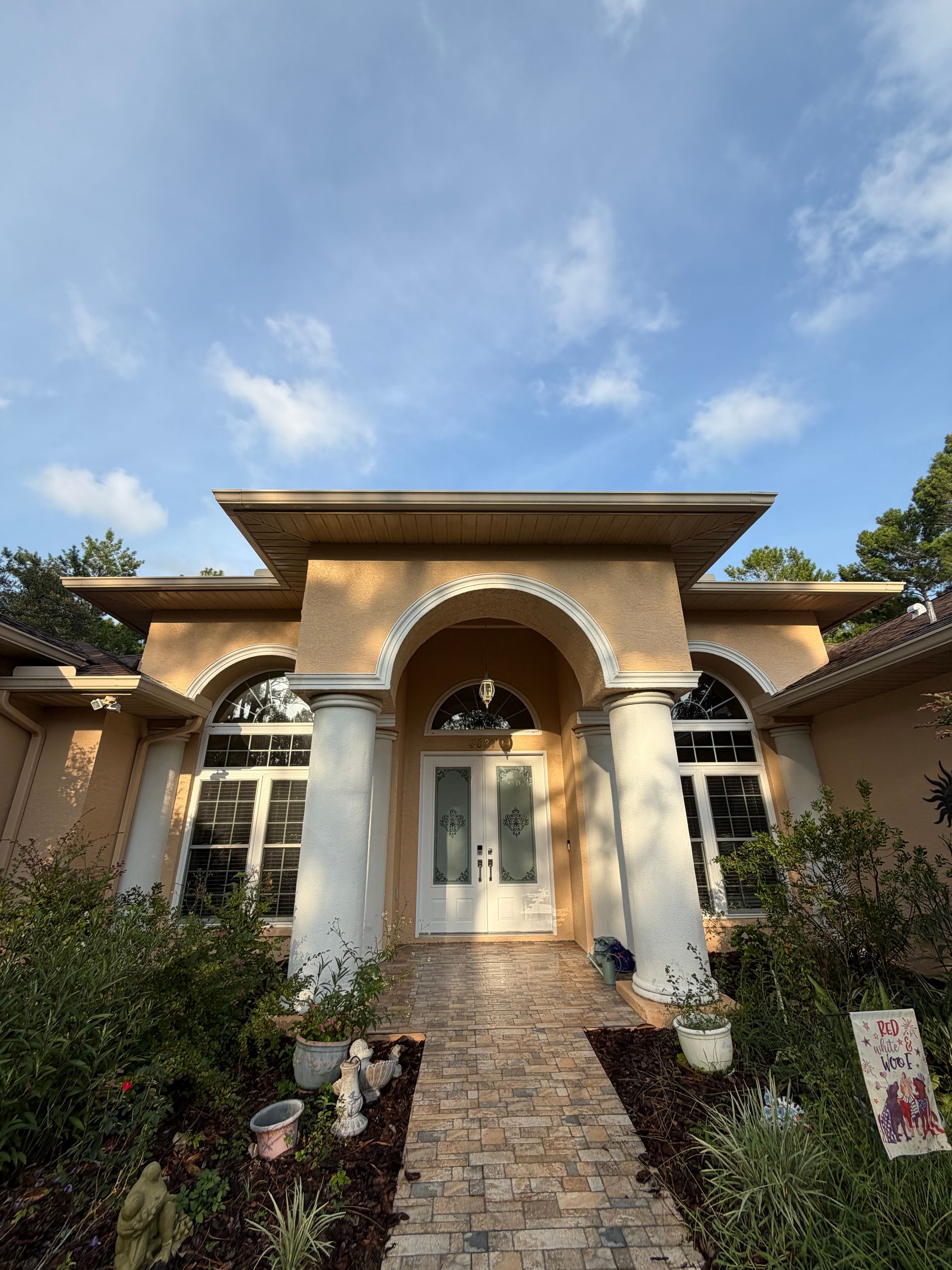 Mediterranean-style house entrance with stone path, arched doorway, and blue sky overhead