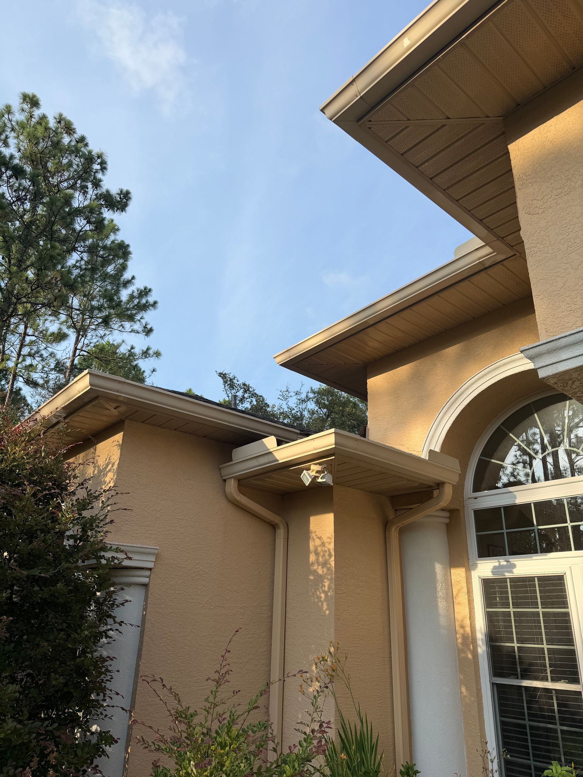 Suburban house exterior with tan stucco walls, arched window, and trees against a blue sky