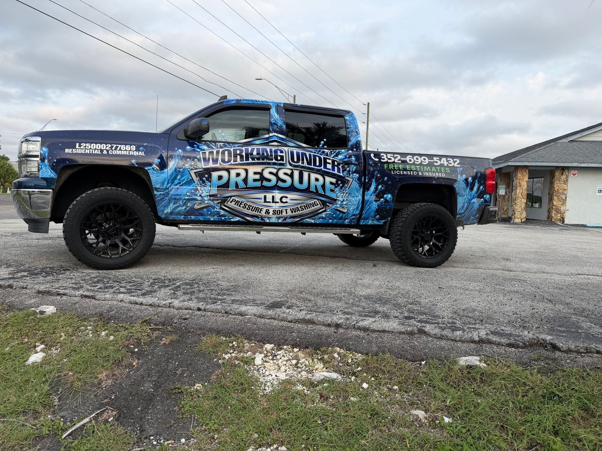 Blue lifted pickup truck with “Pressure” graphics parked on gravel under cloudy sky