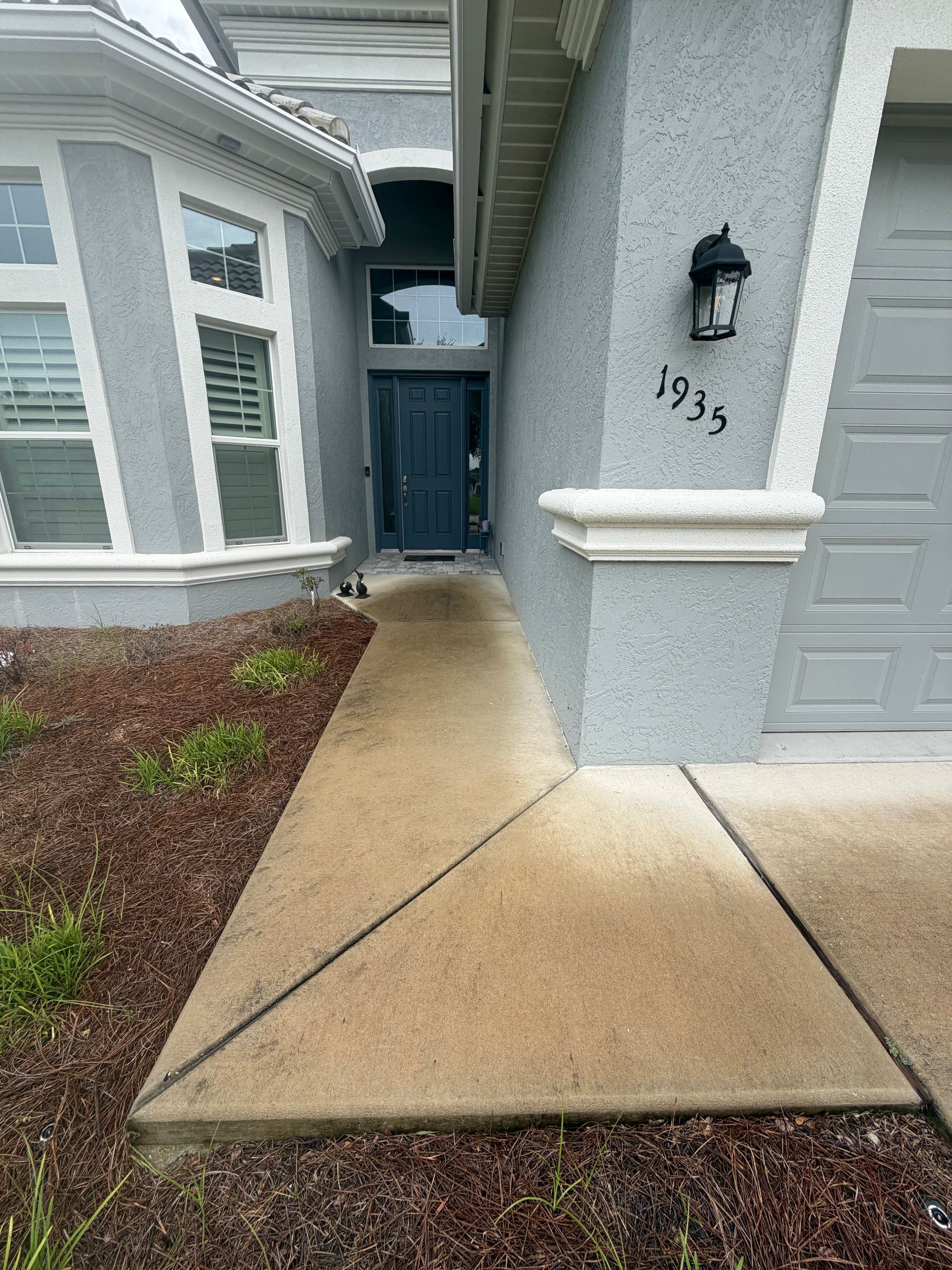 Front walkway beside gray house with blue door and garage, showing a concrete ramp and house number 1935.