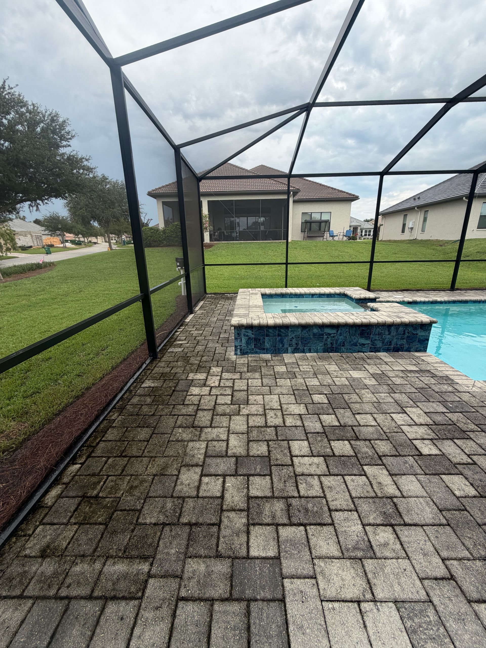 Screened patio with stone pavers and a small blue pool beside a grassy yard and house.