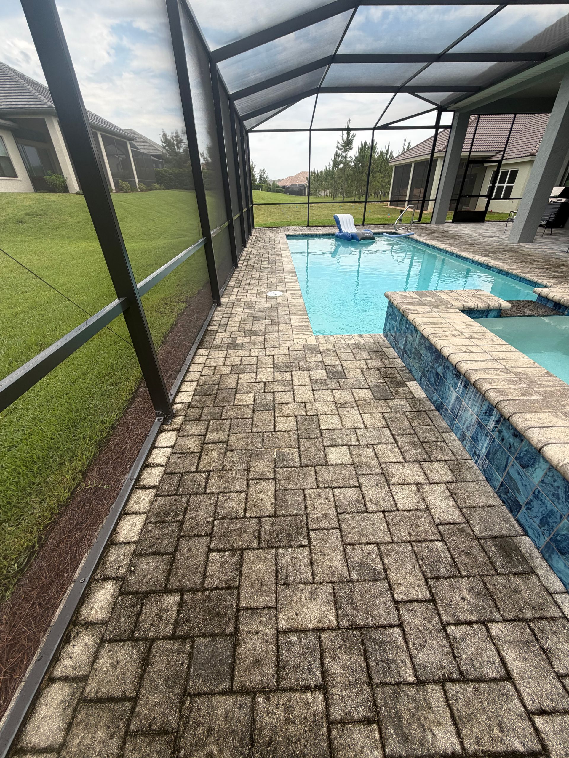Covered pool patio with brick pavers, screened enclosure, and a turquoise swimming pool.