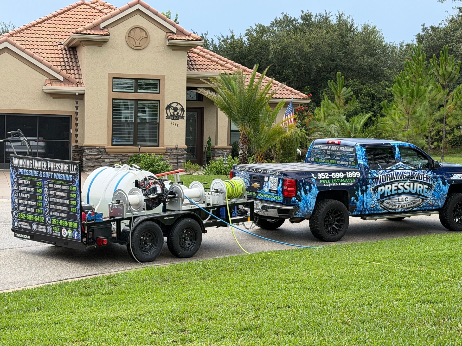 Blue work truck towing a trailer with tanks in front of a suburban house and lawn