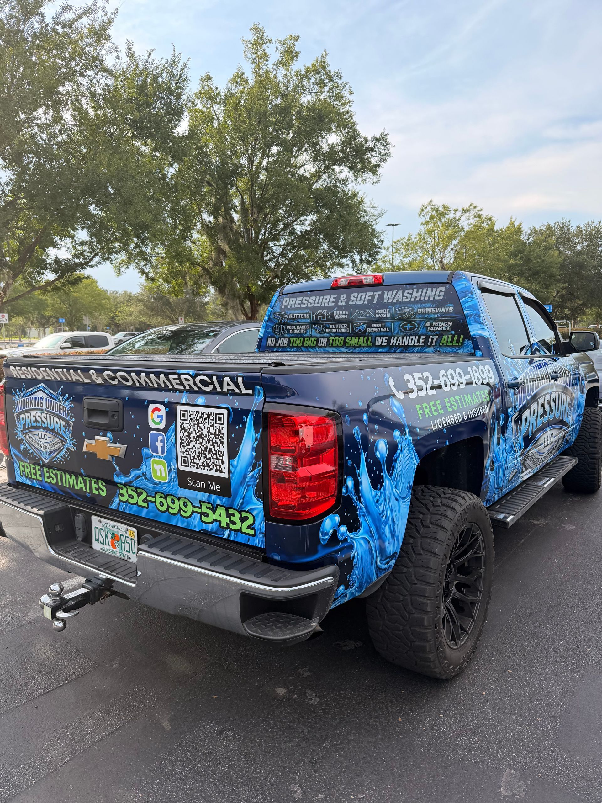 Blue lifted pickup truck covered in promotional graphics and QR codes parked outdoors