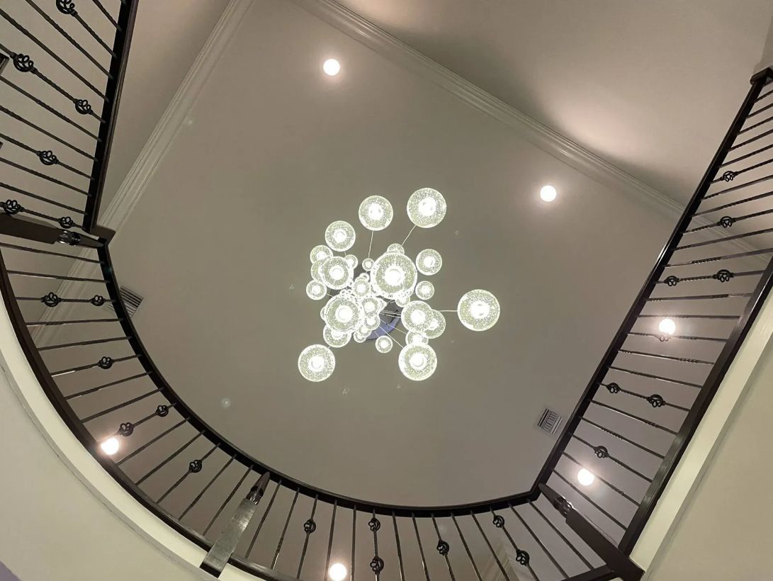 View up a stairwell with curved black railings and a modern chandelier on the ceiling