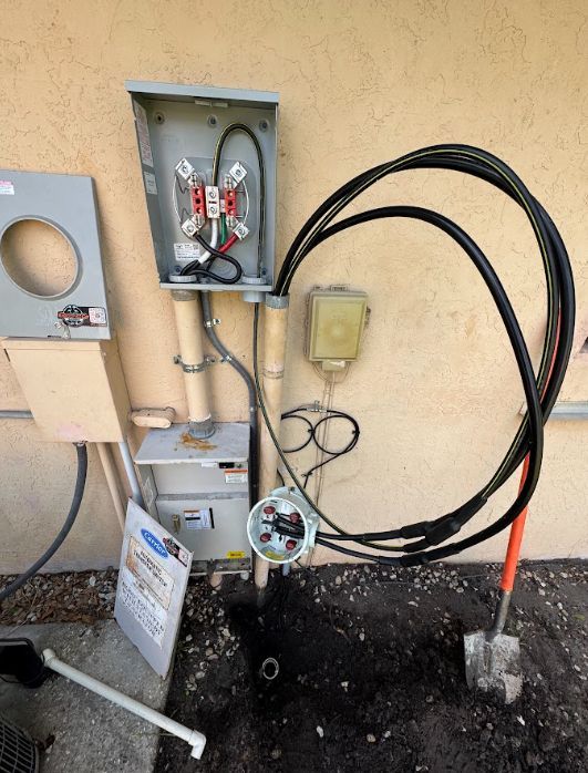 Outdoor electrical utility boxes and cables mounted on a beige wall, with a coiled black cable and meter below.