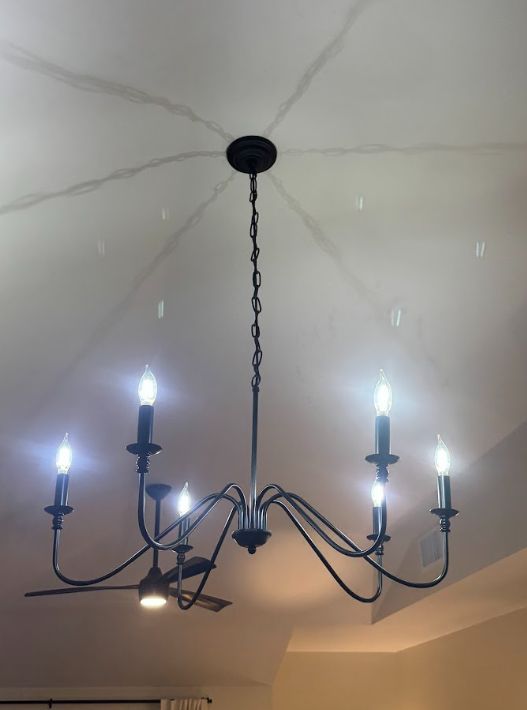 Black metal chandelier with lit candle-style bulbs hanging from a white ceiling