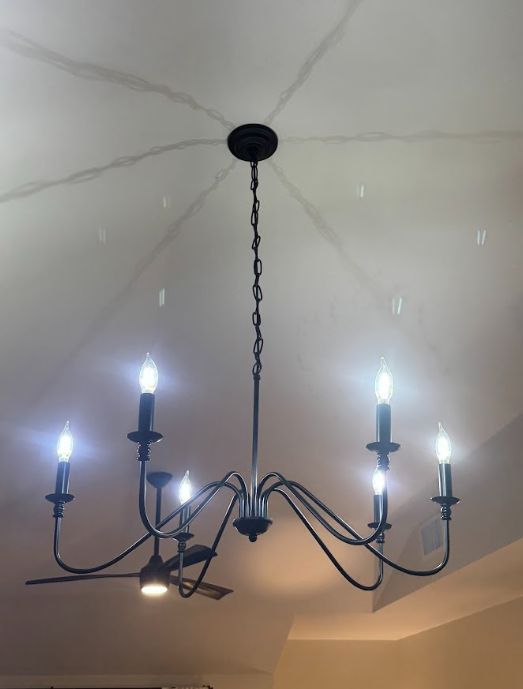 Black chandelier with lit candle-style bulbs on a white ceiling inside a room