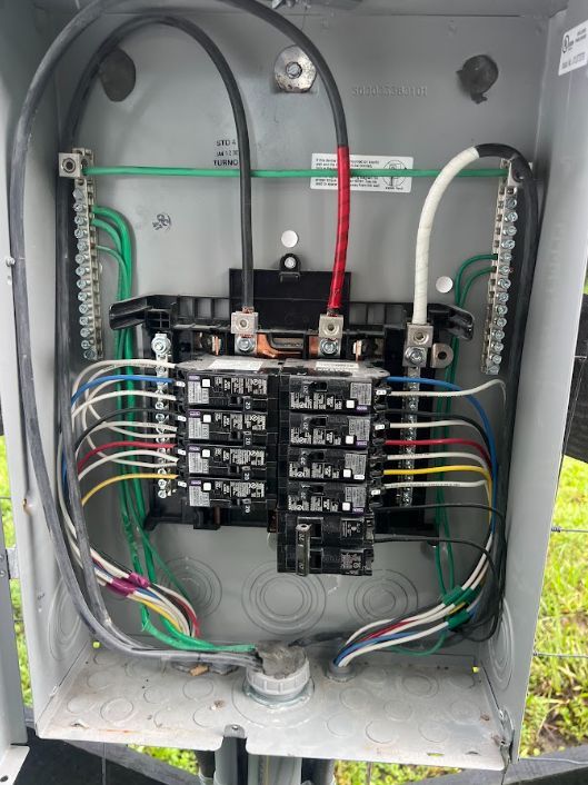 Open electrical breaker panel with wiring and two large cables inside a gray metal box
