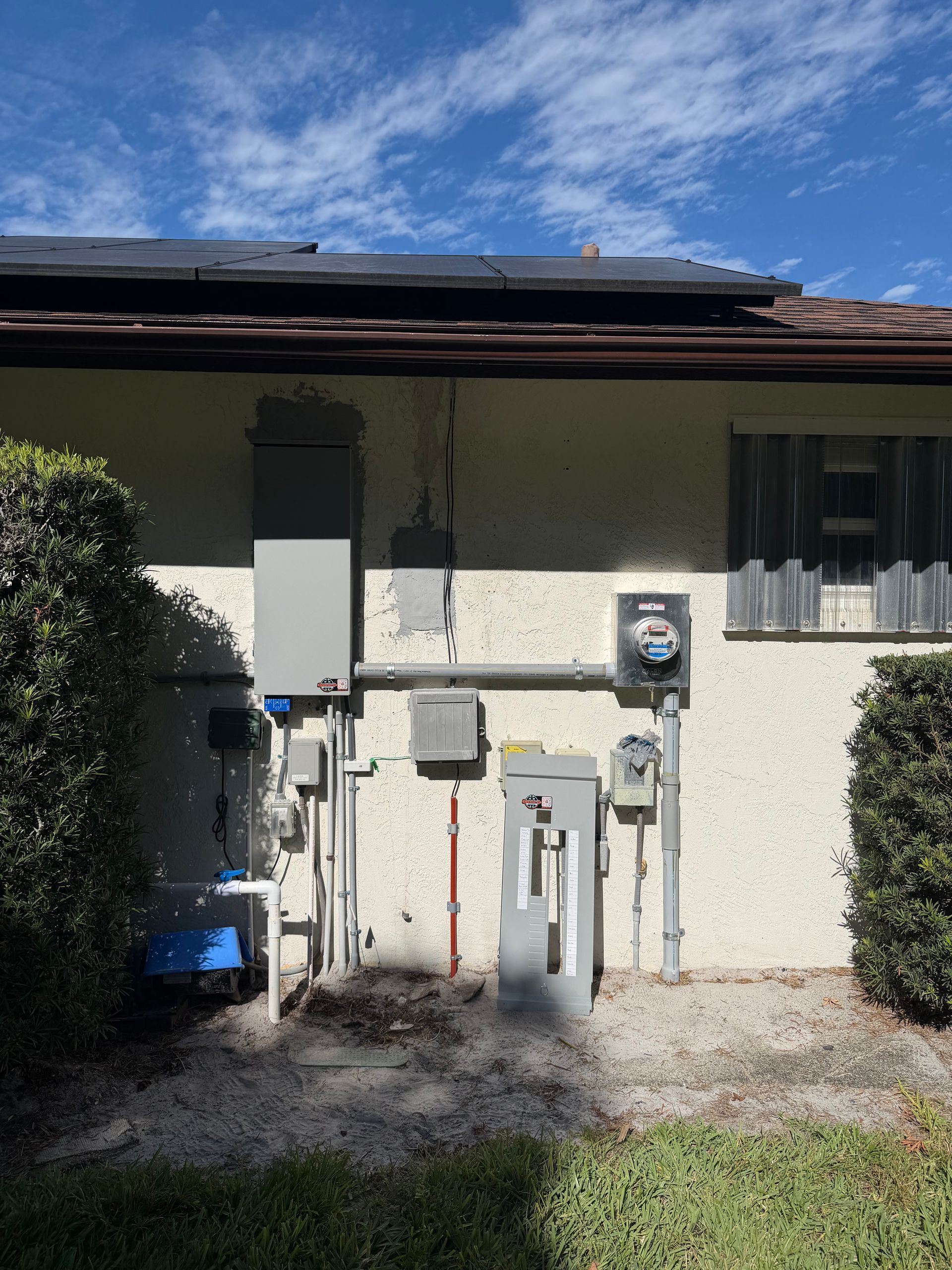 Exterior wall with utility meters, pipes, and a window under a roof overhang.