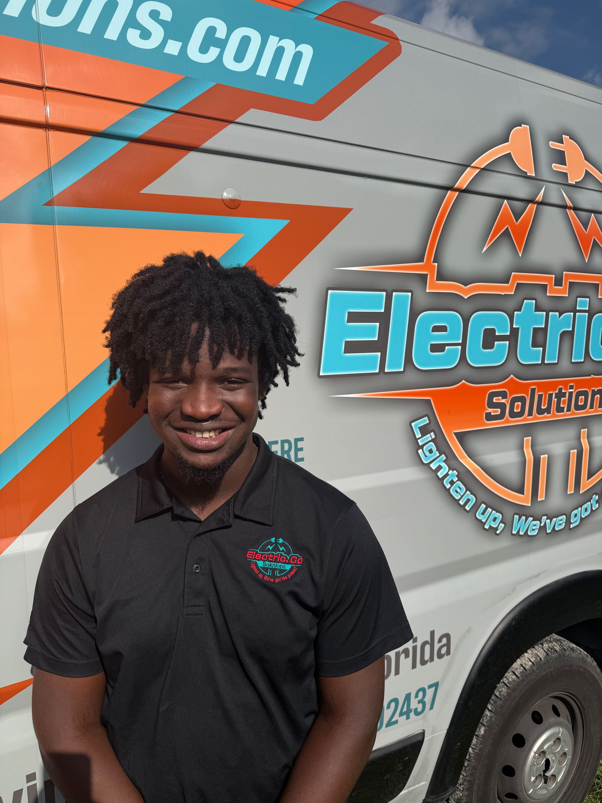 Smiling person in black polo standing beside a colorful electric service van with company logo.