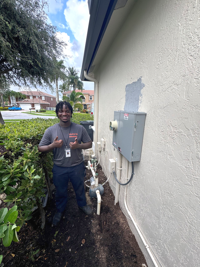 Person standing beside outdoor utility boxes and pipes next to a house wall in a narrow side yard.