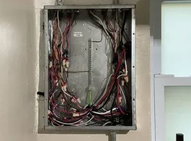 Open electrical panel with exposed tangled wires in a wall recess