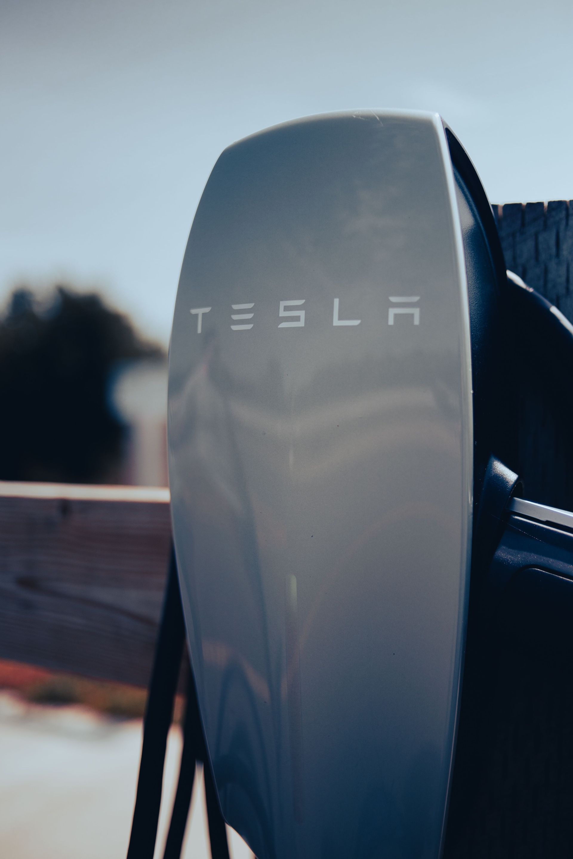 Tesla charging connector on a vehicle, with white Tesla logo on a gray panel.