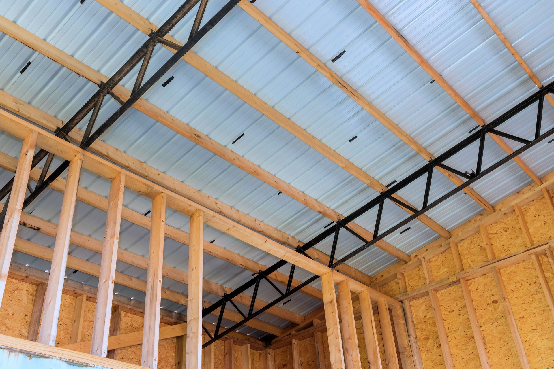 Interior of a building under construction, showing wooden frame walls, metal roof, and black steel trusses.
