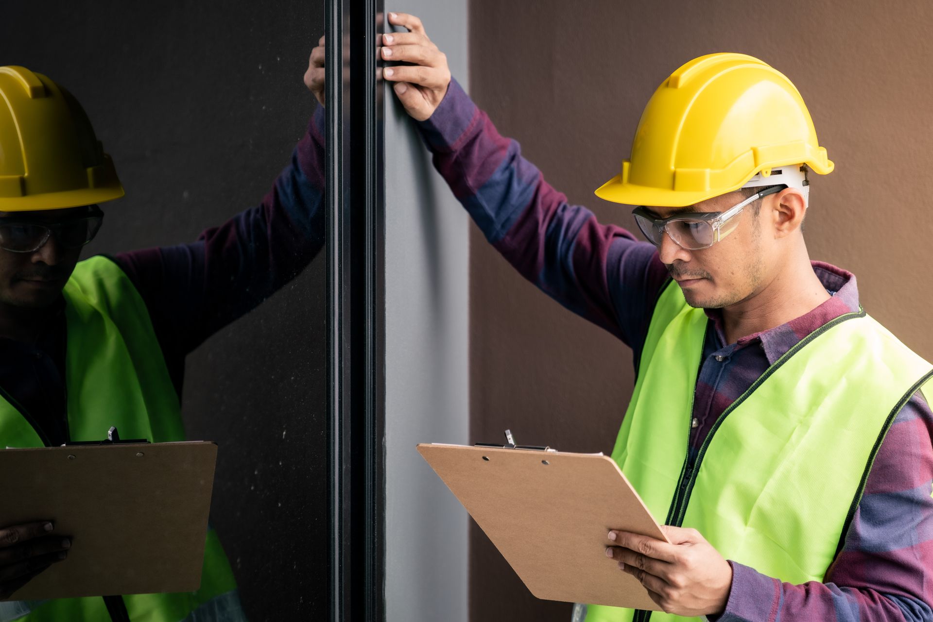 Inspector in a yellow helmet and vest examining a dark surface, holding a clipboard.