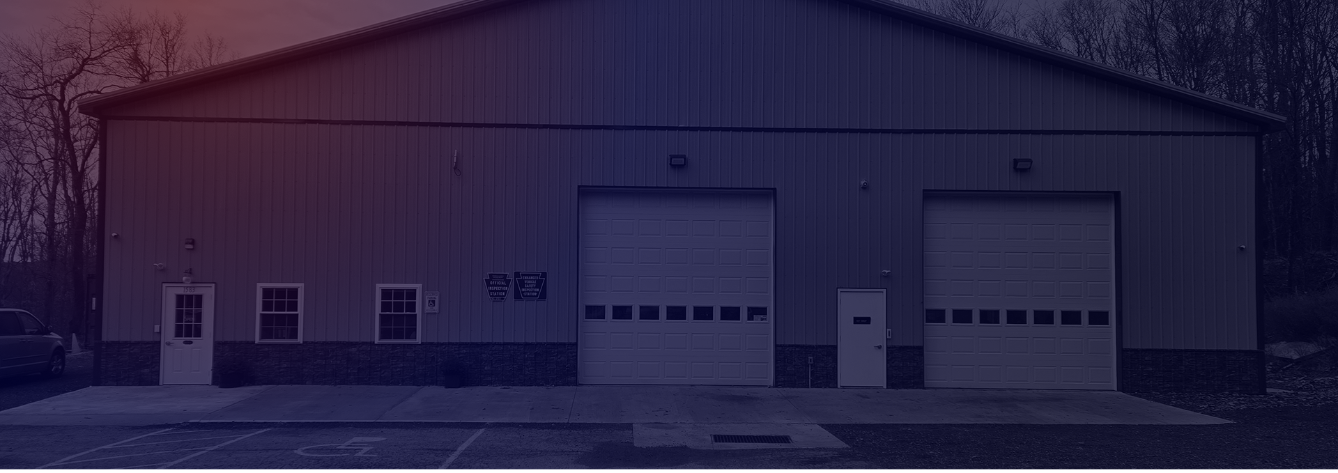 Dark industrial warehouse with two large white garage doors and small side windows. | Hauger's Automotive Services