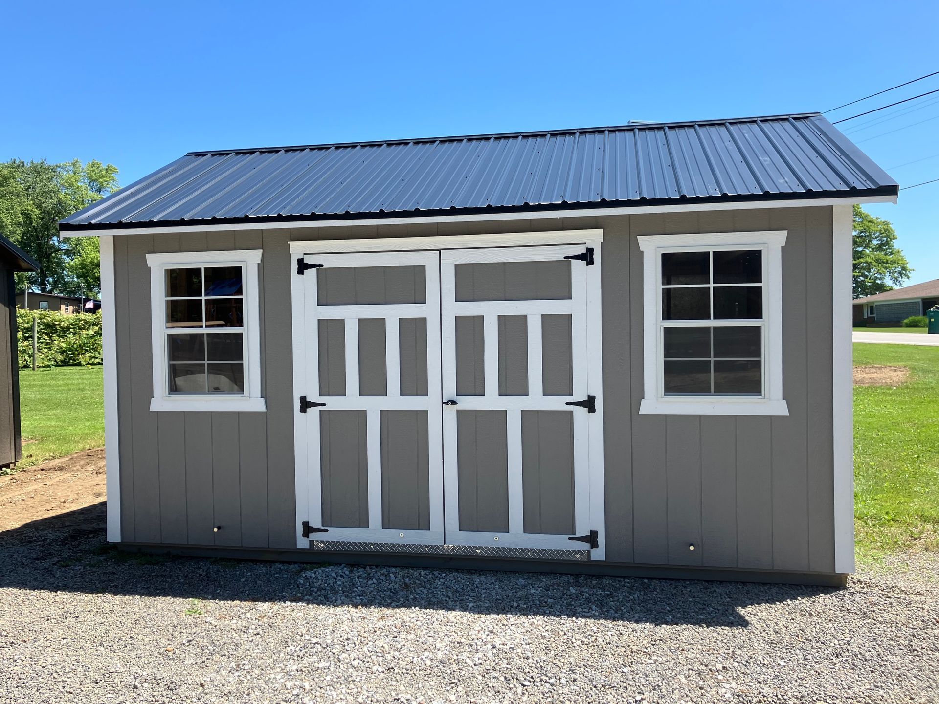 Gray shed with white trim, black roof, and double doors, sitting on gravel.