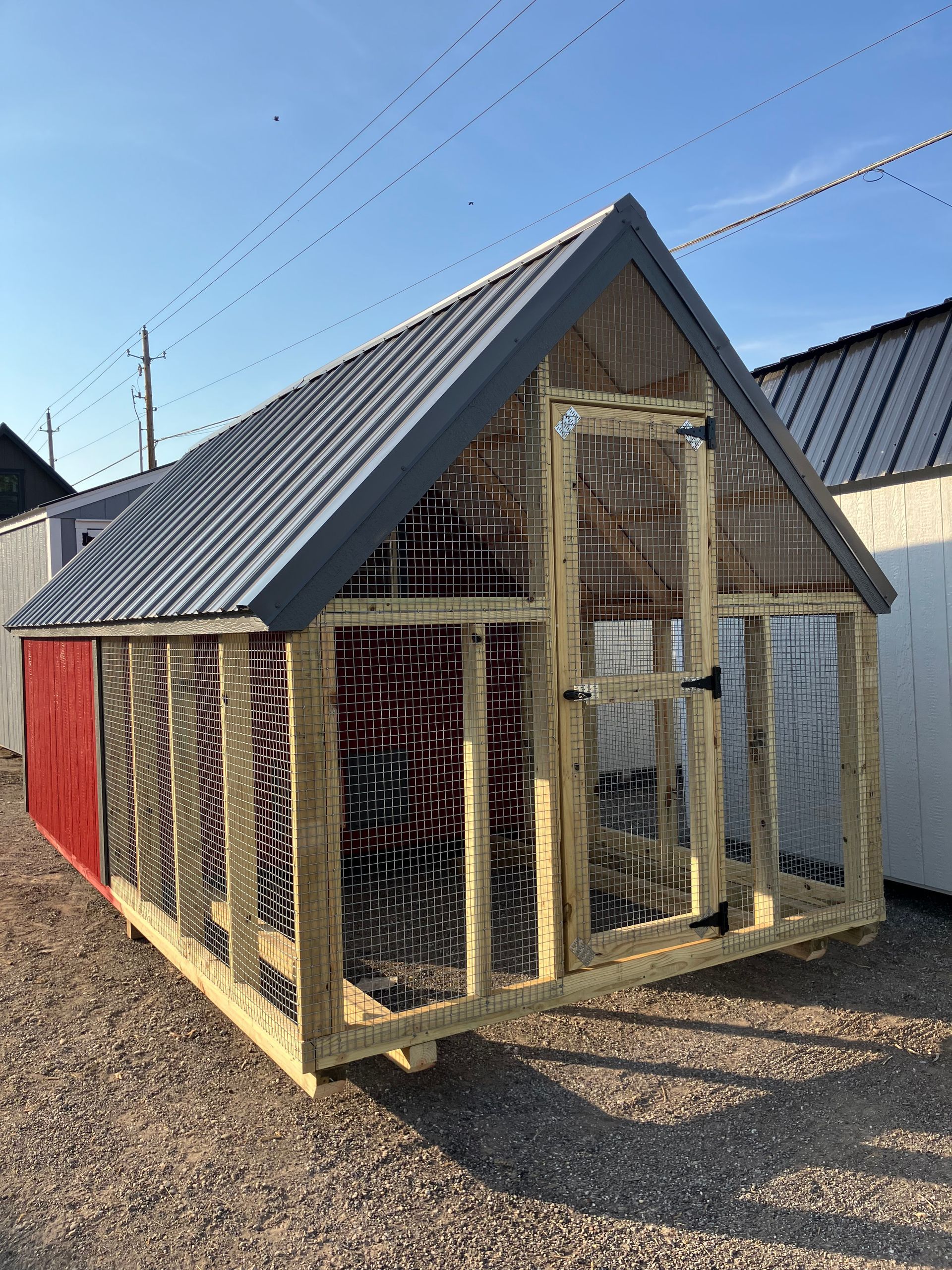 Chicken coop with wire mesh walls and a metal roof, red side.