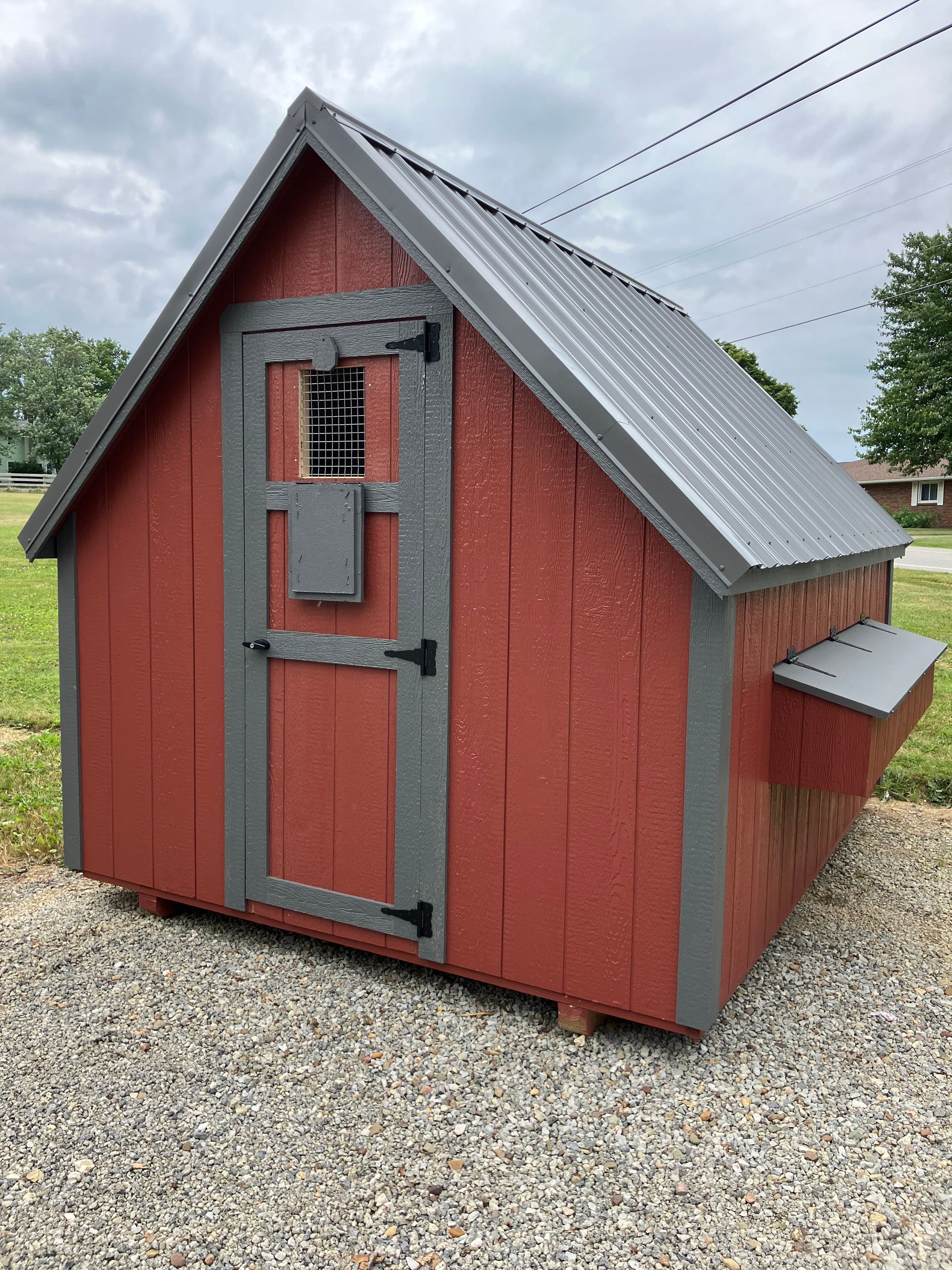 Red and gray chicken coop with a gray metal roof, sitting on gravel.
