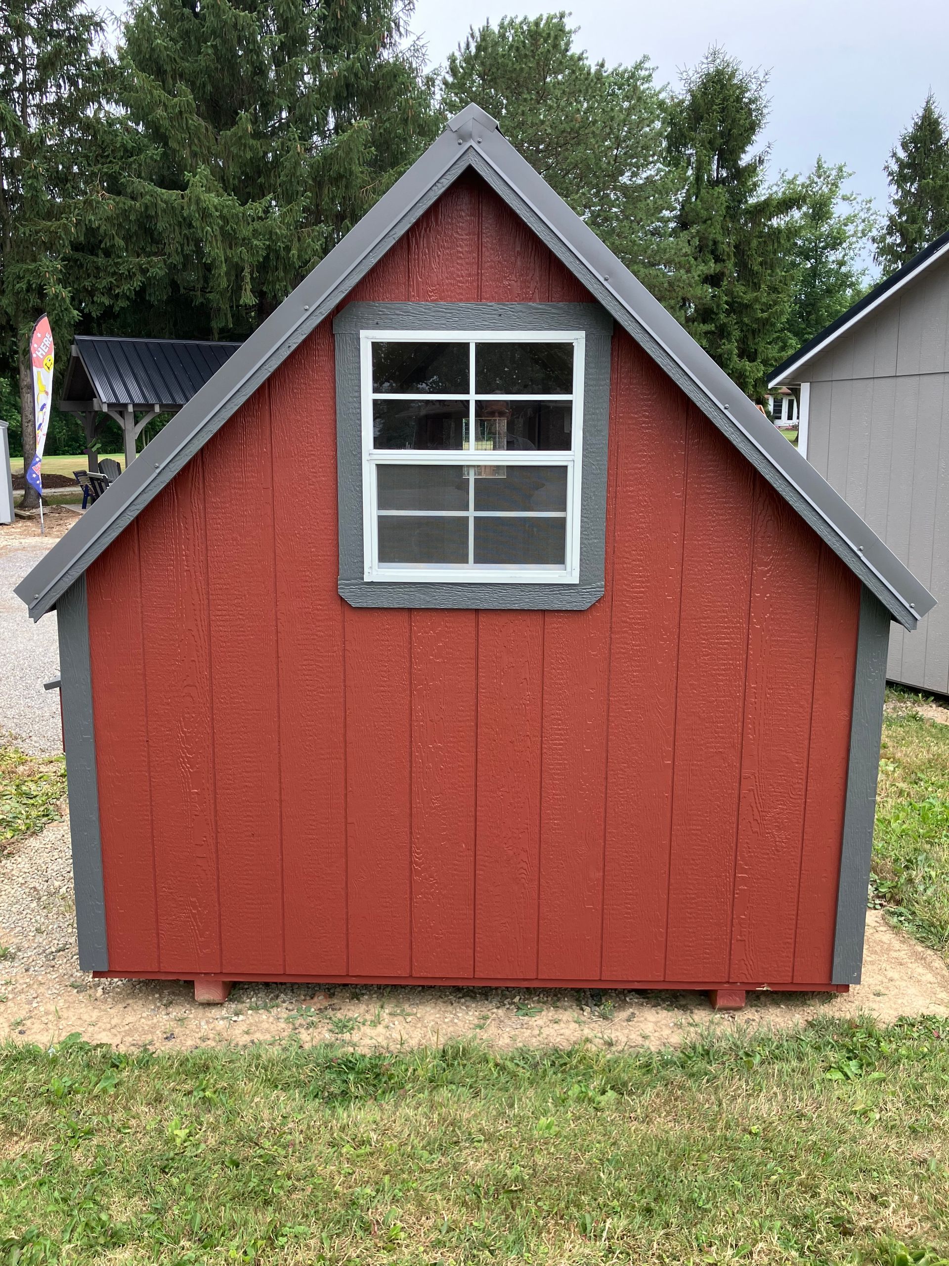 Red shed with gray trim, a window, and a gray roof, set on gravel with grass in the foreground.