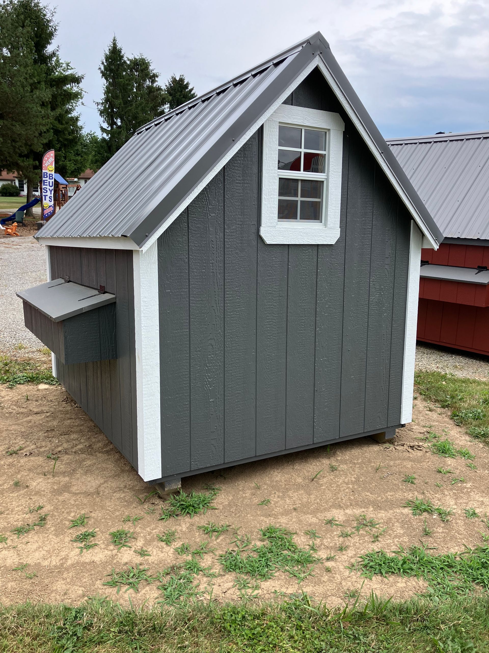 Gray chicken coop with white trim, a metal roof, and a small window.