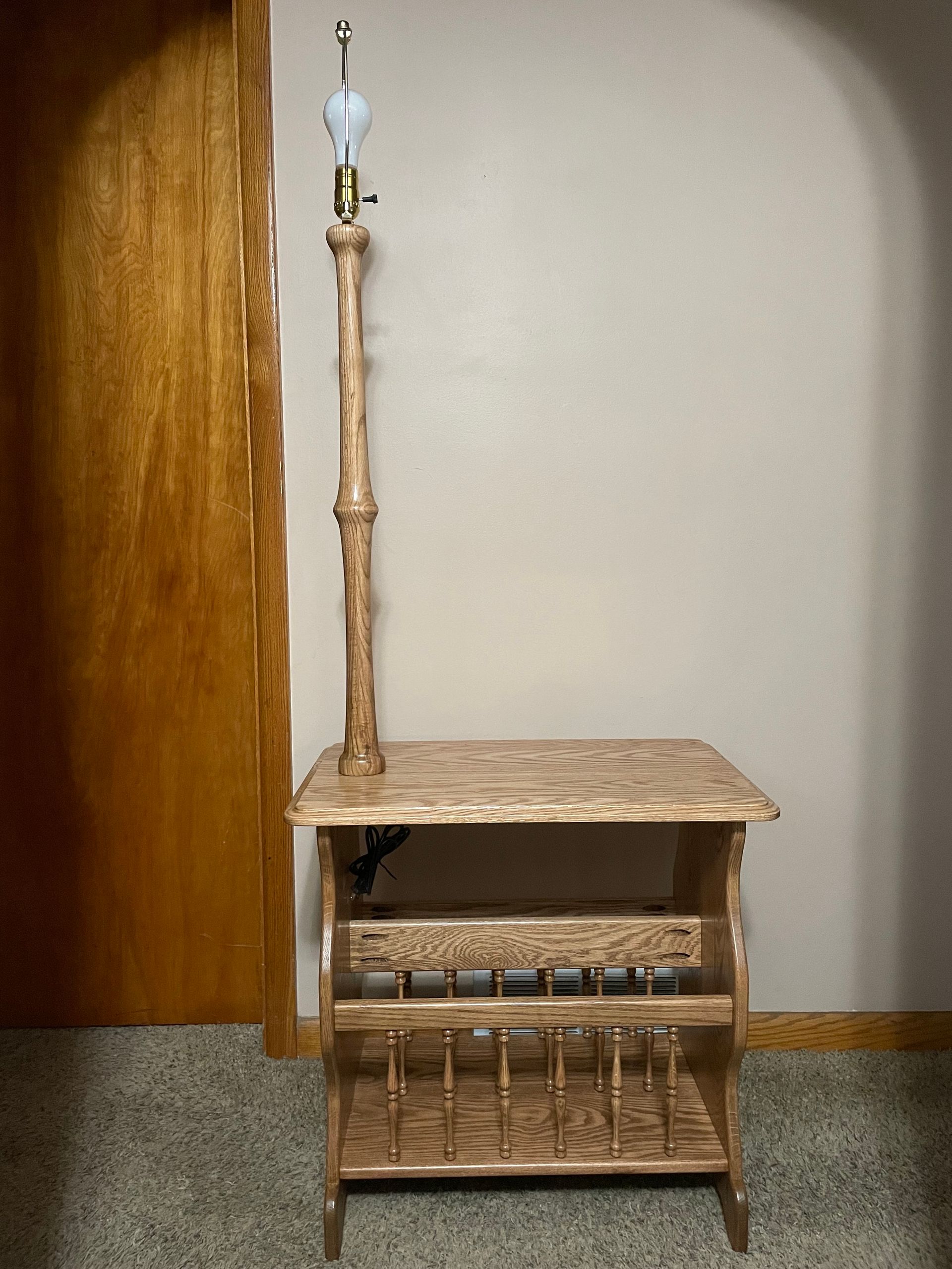 Wooden lamp with a magazine rack, standing in a room with a closed wooden door.